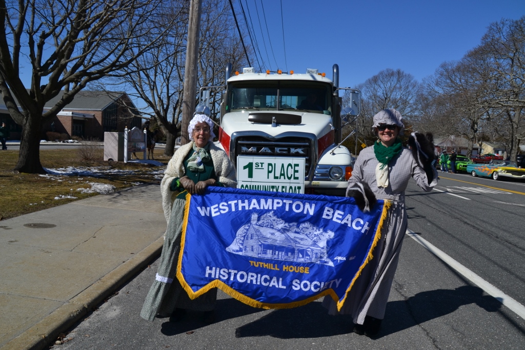 Two women in historical costumes holding a banner for the Westhampton Beach Historical Society, standing in front of a large truck with a '1st Place Community Float' sign.