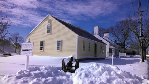 A historical building covered in snow with a cannon in the foreground, under a clear blue sky.